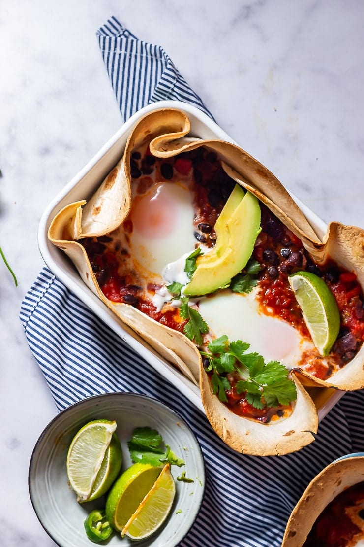 Overhead shot of huevos rancheros baked eggs on a striped cloth and marble background