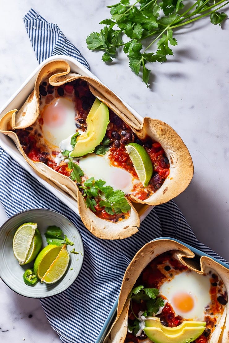 Overhead shot of huevos rancheros baked eggs on a striped cloth and a marble background