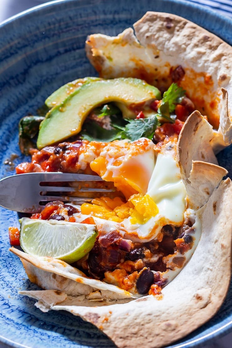 Portion of huevos rancheros baked eggs in a blue bowl with a fork 