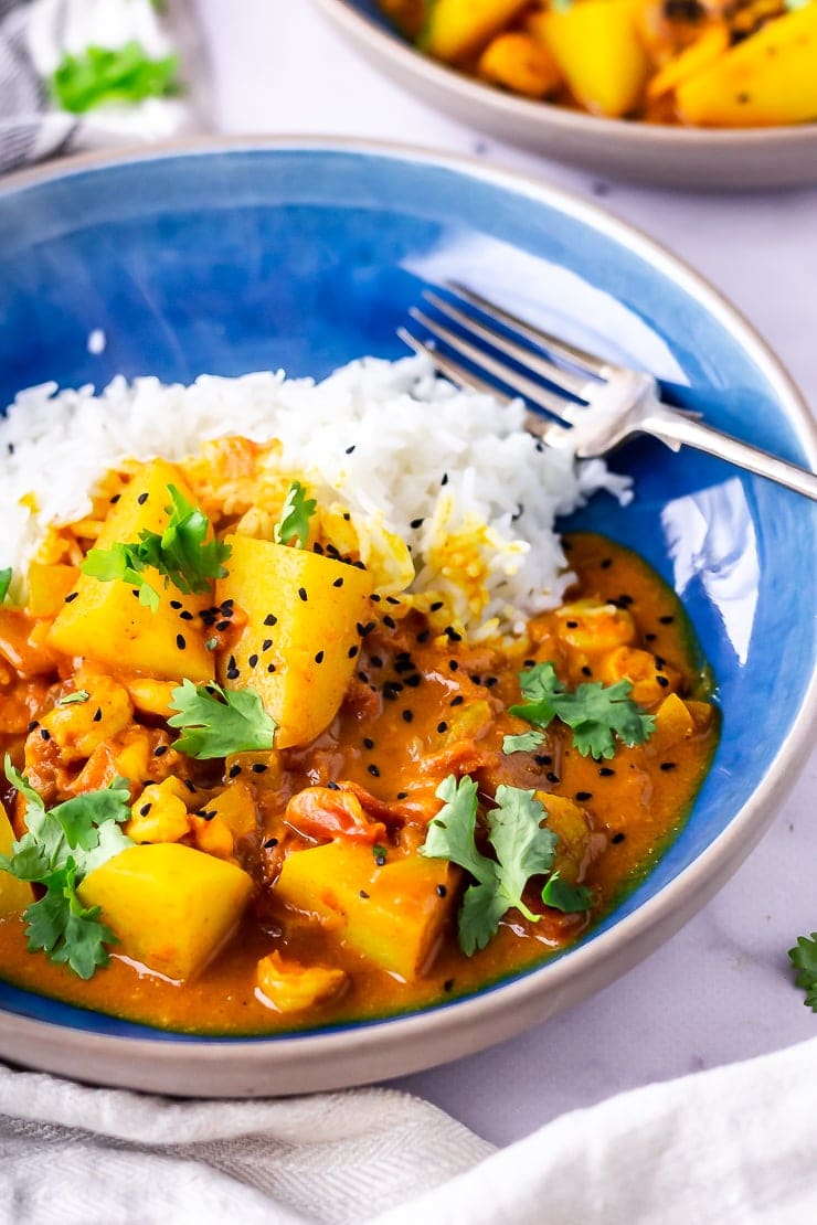 Side angle shot of creamy prawn curry with rice and a fork in a blue bowl