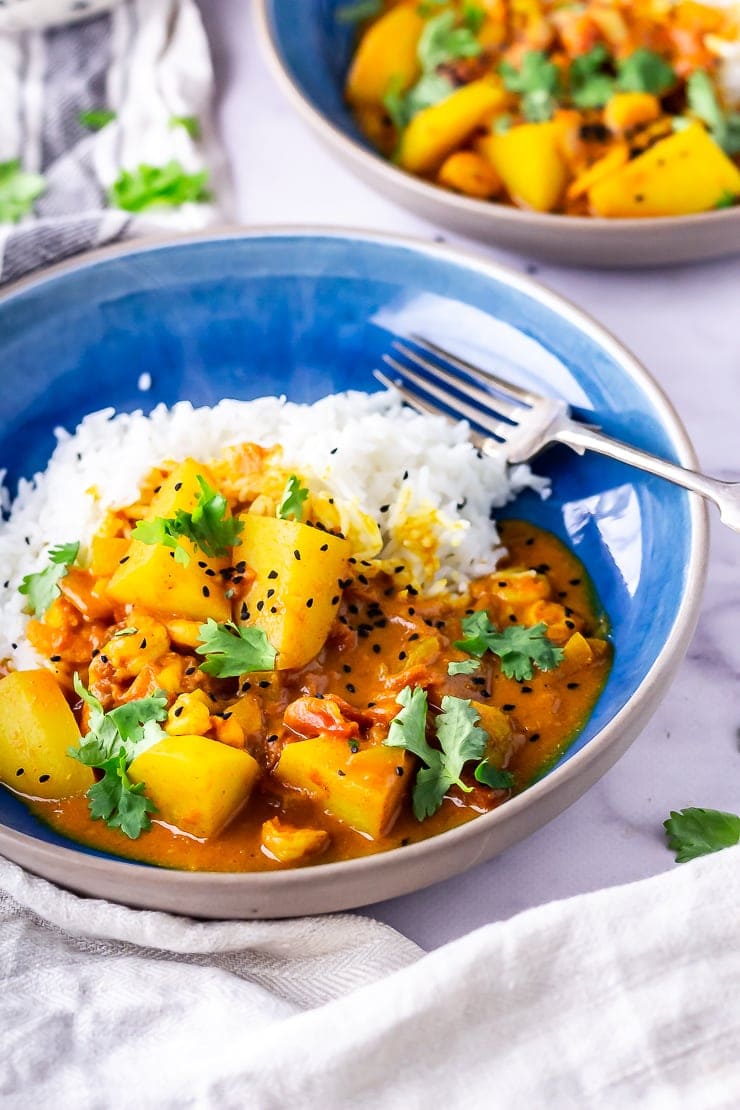 Side angle shot of creamy prawn curry with rice in a blue bowl with a fork