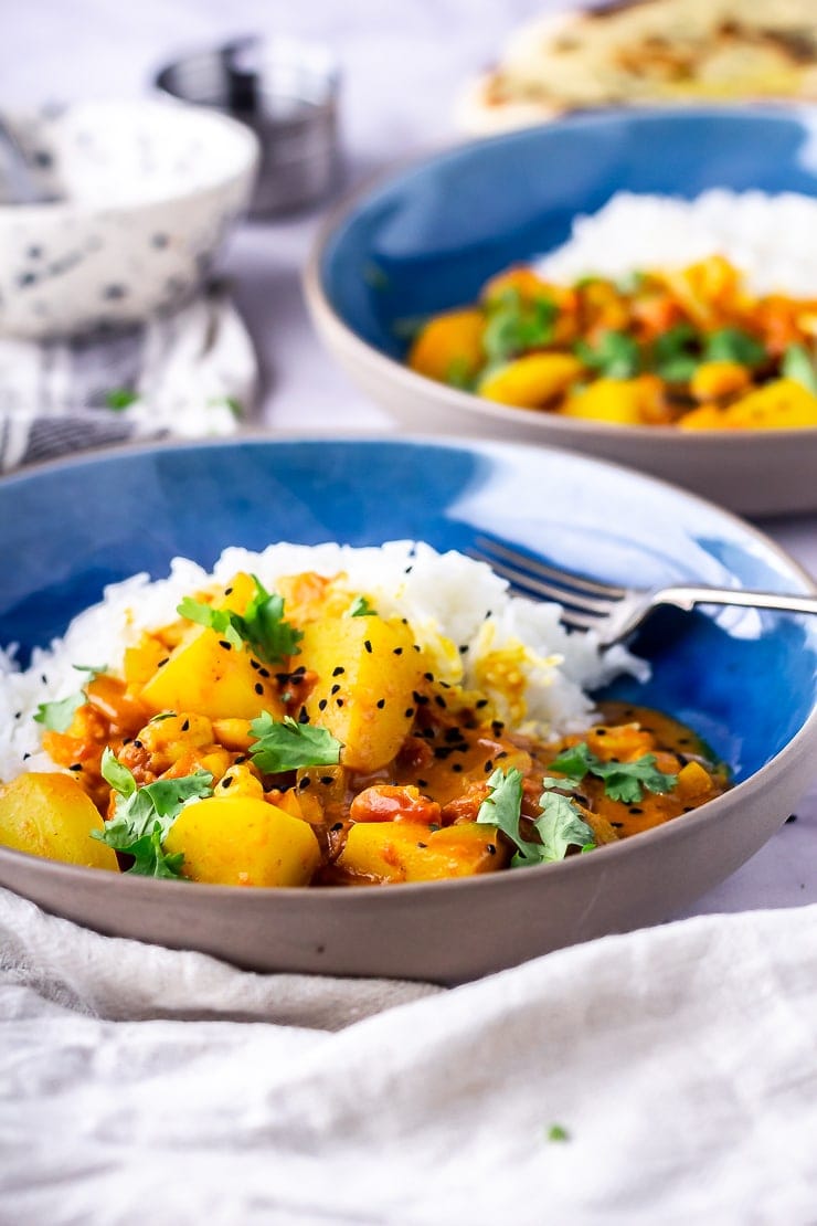 Side angle shot of creamy prawn curry with rice in a blue bowl with a cloth