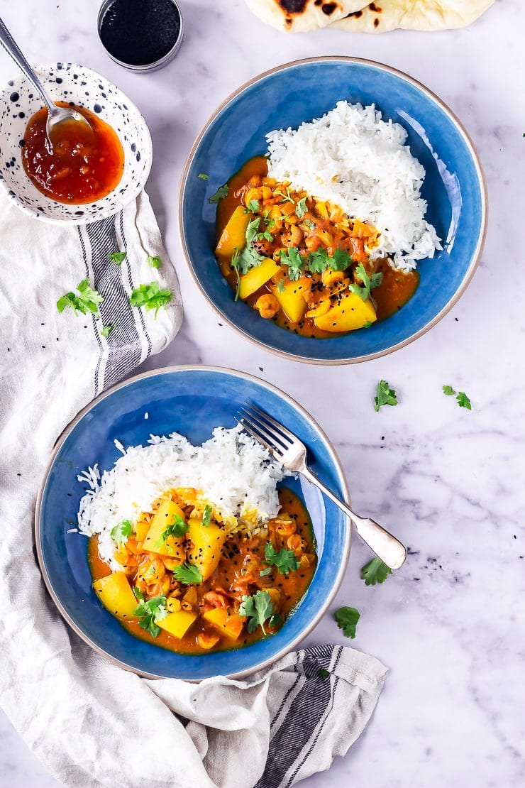 Overhead shot of two bowls of prawn curry with rice on a marble background