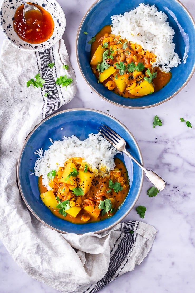 Overhead shot of two bowls of creamy prawn curry with potato on a marble background with a cloth