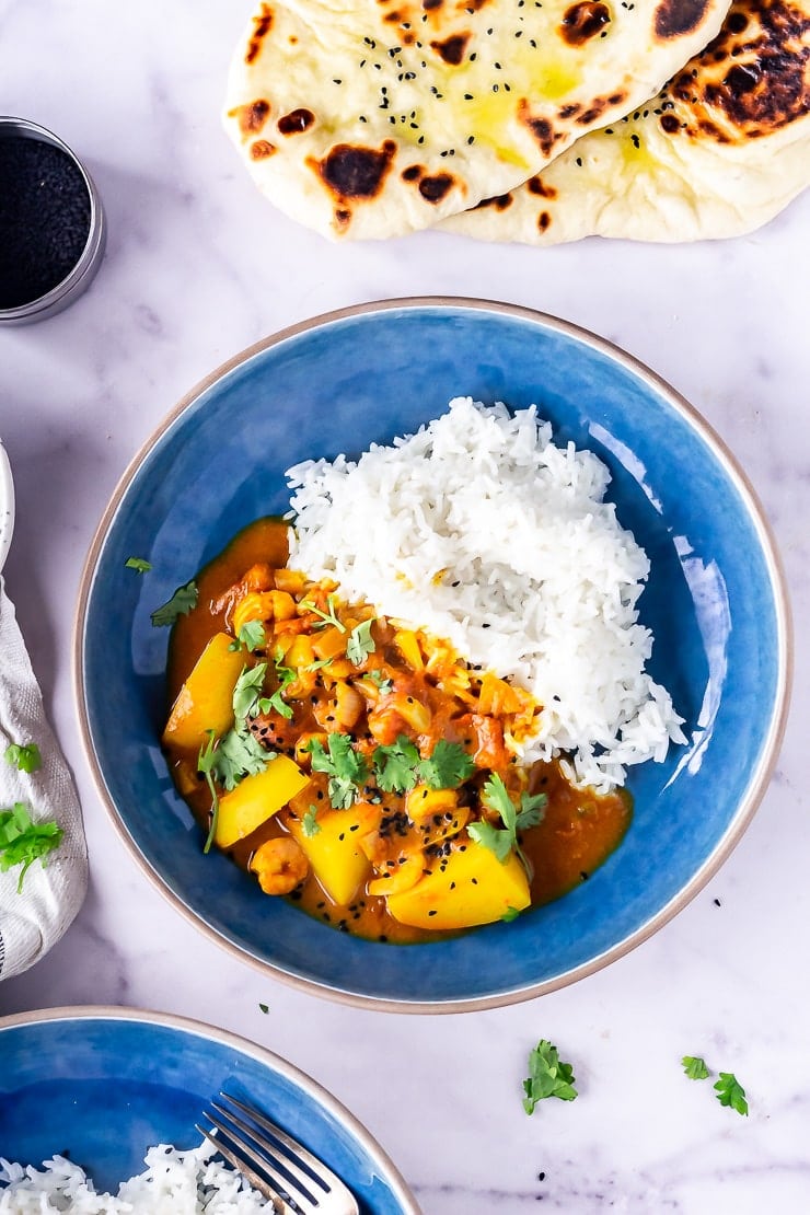 Overhead shot of creamy prawn curry with potato in a blue bowl on a marble background