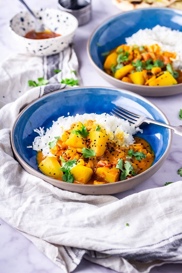 Side angle shot of creamy prawn curry in a blue bowl with a cloth