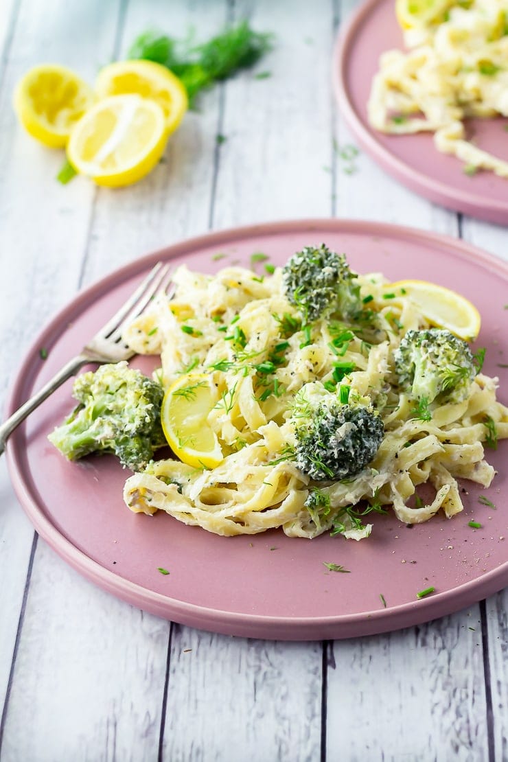 Side angle shot of salmon pasta with broccoli on a pink plate over a white wooden background