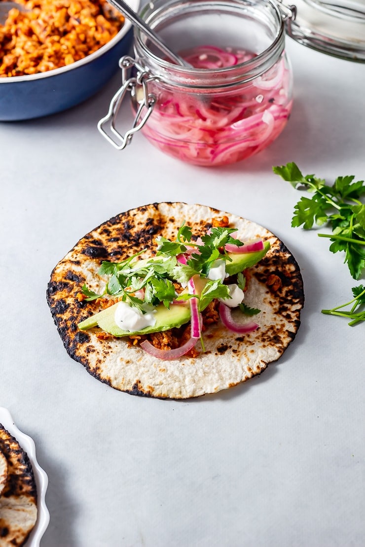 Shot of salmon tacos on a grey background with a jar of pickled onions in the background