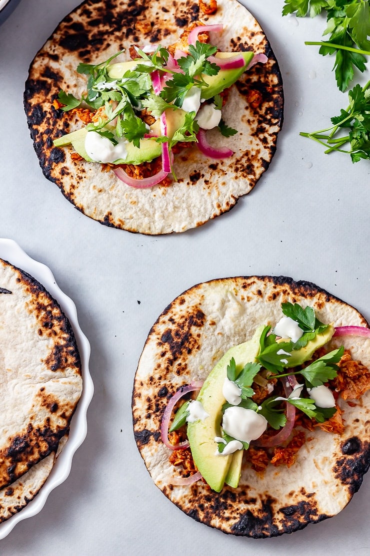 Overhead shot of two salmon tacos on a grey background with avocado and coriander