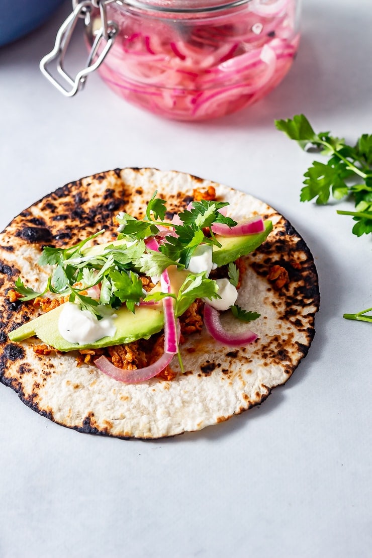 Side on shot of salmon tacos on a grey background with pink pickled onions