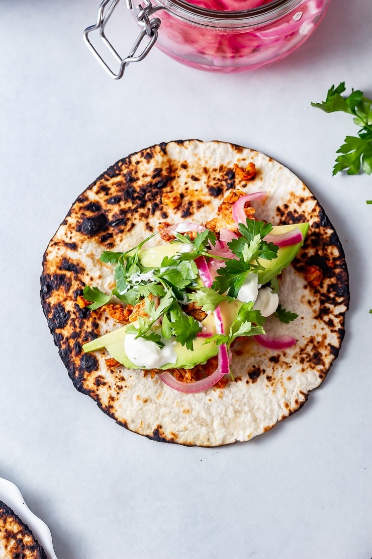 Overhead shot of salmon tacos on a grey background with pickled red onions