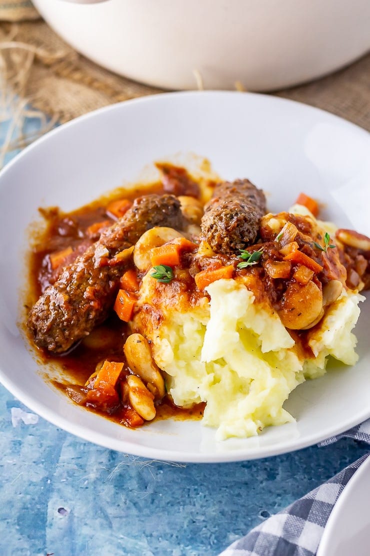 White bowl of vegetarian sausage casserole with mash on a blue background