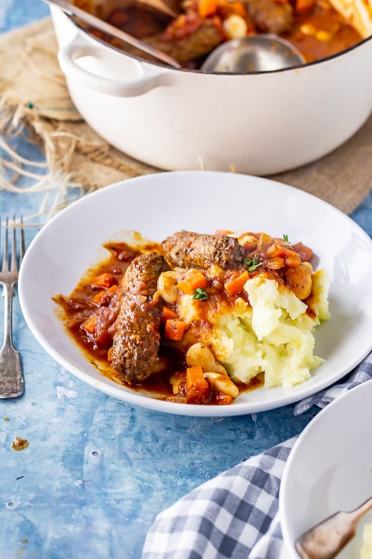 Side angle shot of vegetarian sausage casserole in a white bowl on a blue background