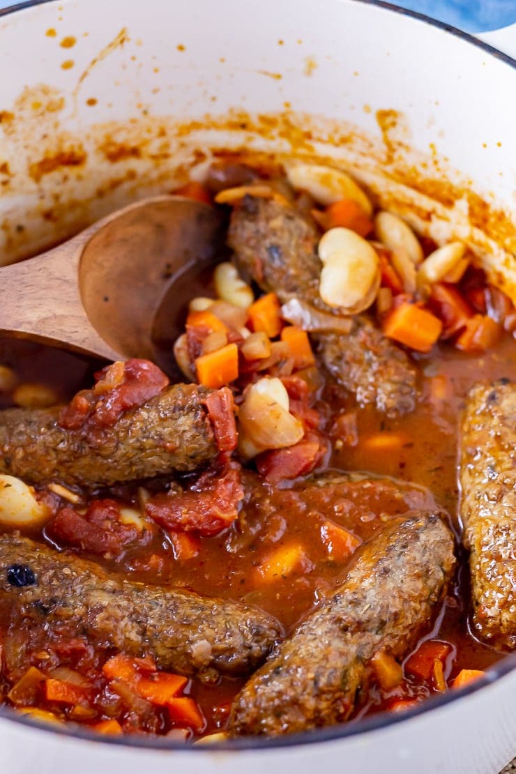 Vegetarian sausage casserole in a white pot with a wooden spoon