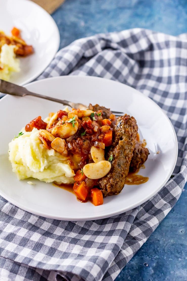 White plate of vegetarian sausage casserole with mash on a checked cloth