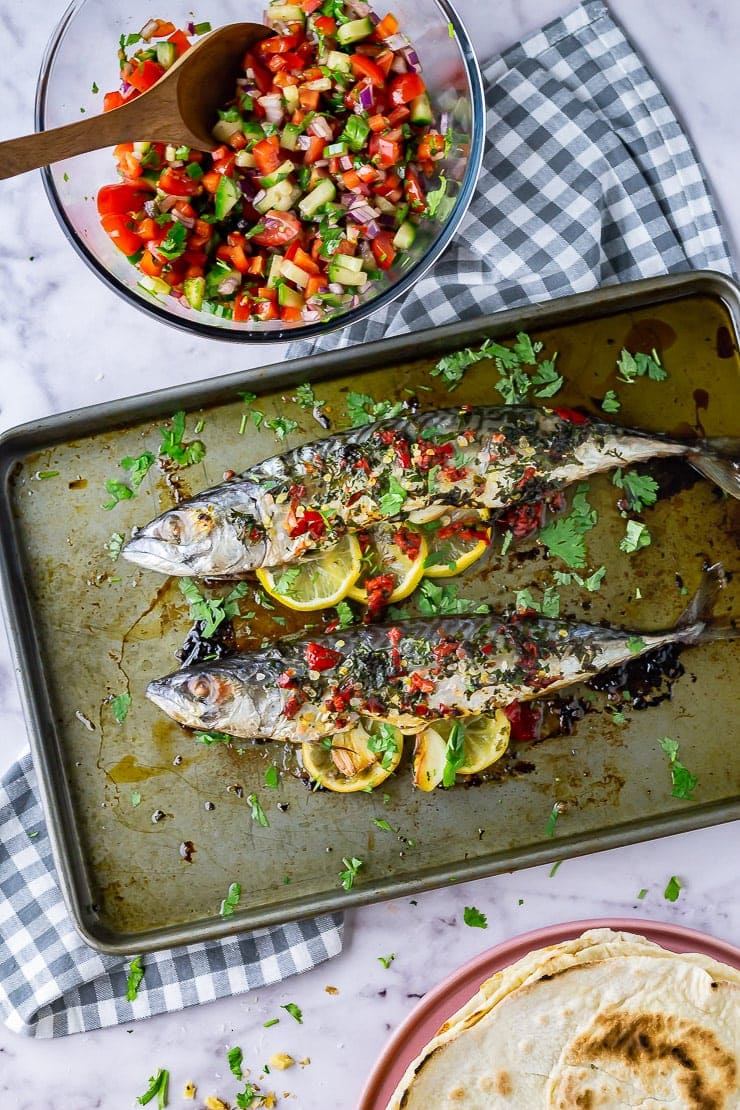 Overhead shot of whole baked mackerel on a baking sheet with a checked cloth