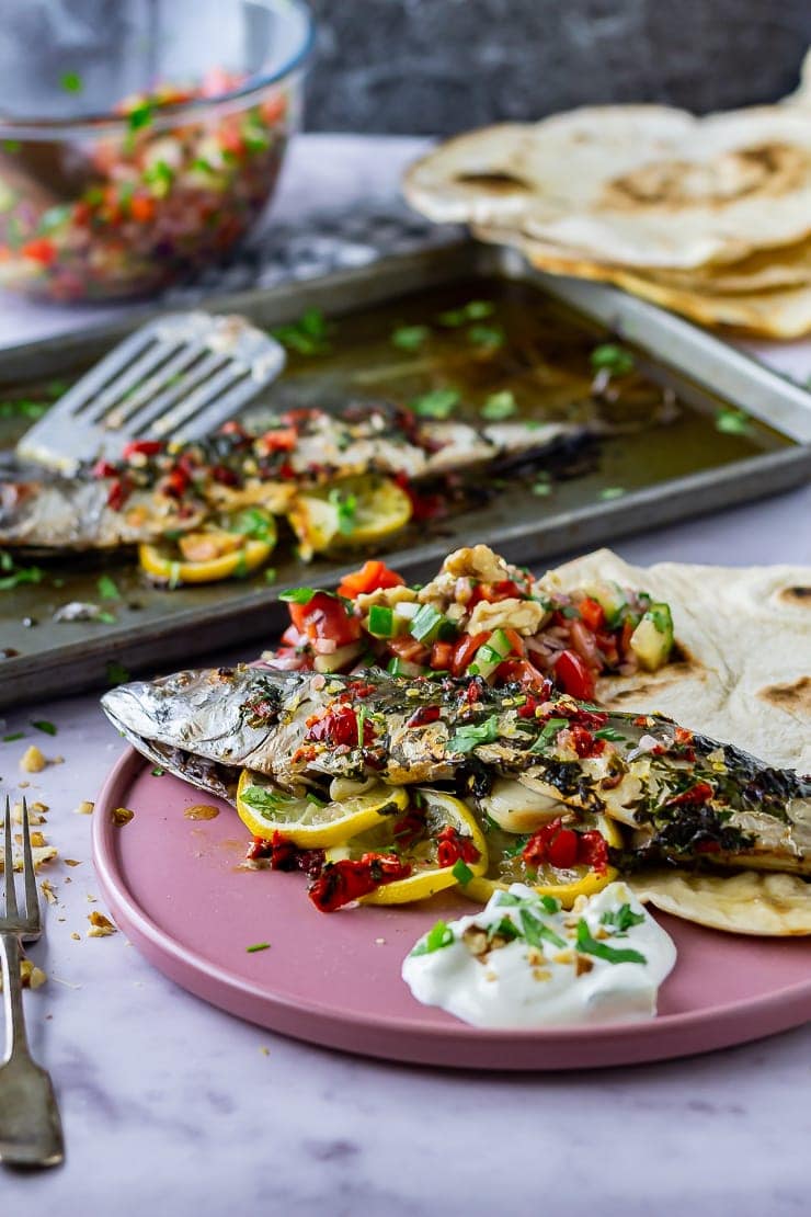 Whole baked mackerel on a pink plate with salad and flatbread