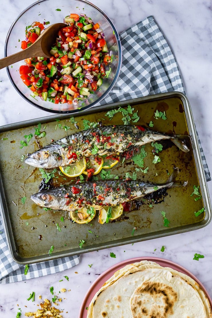 Overhead shot of baked mackerel on a baking sheet on a checked cloth and marble background