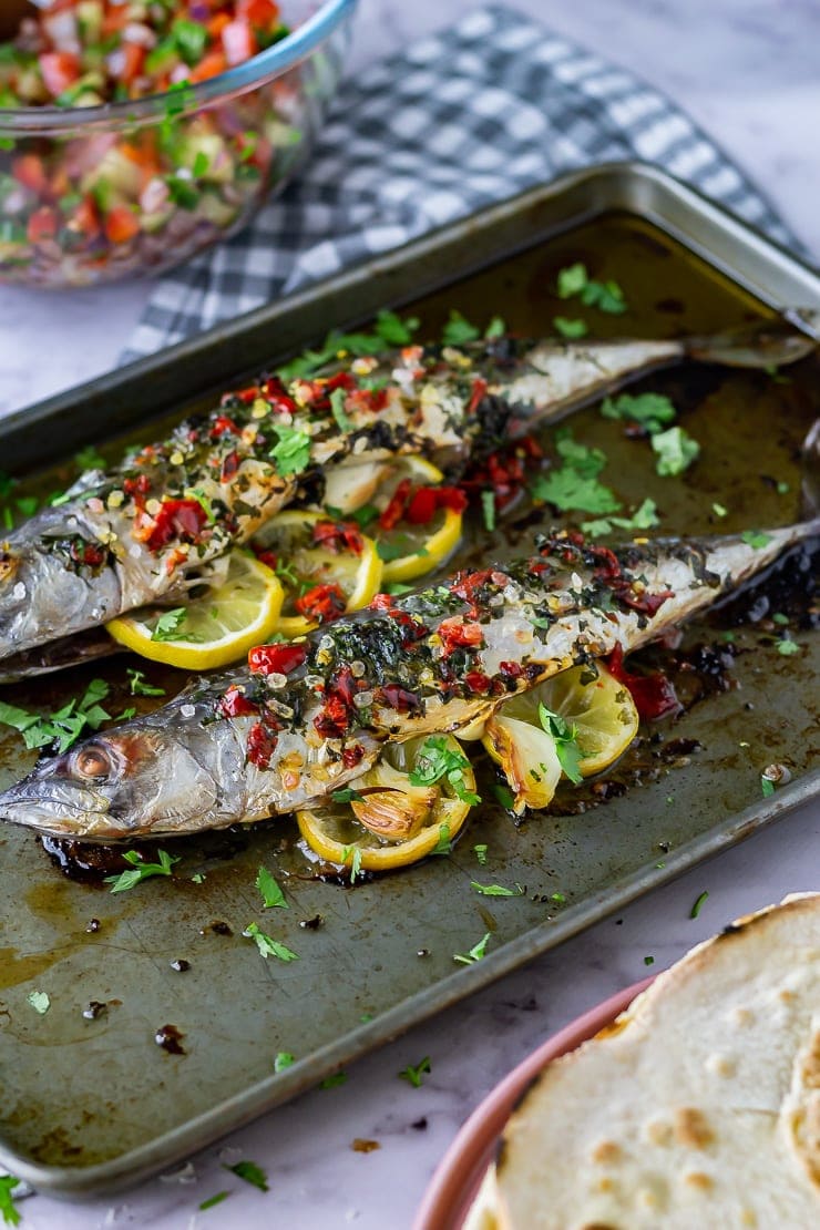 Side on shot of baked mackerel on a baking sheet with a checked cloth