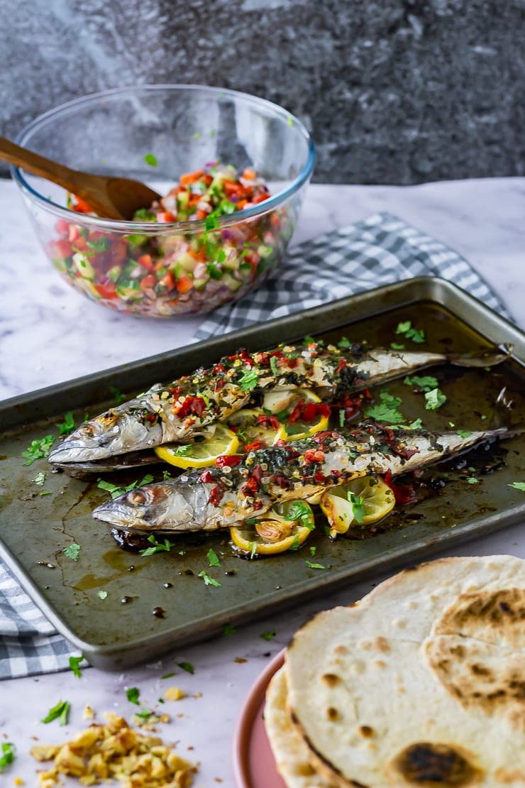 Zoomed out shot of baked mackerel on a baking sheet with salad and flatbreads