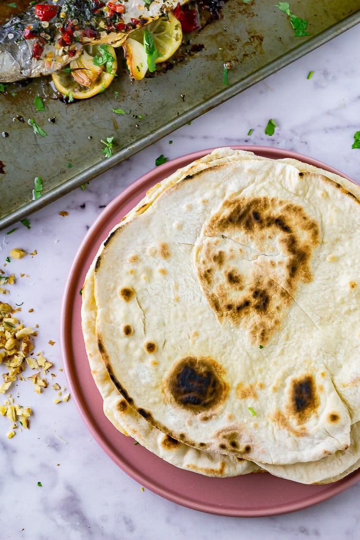 Overhead shot of flatbreads to go with baked mackerel on a pink plate over a marble background