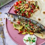 Baked mackerel on a pink plate with salad and flatbread