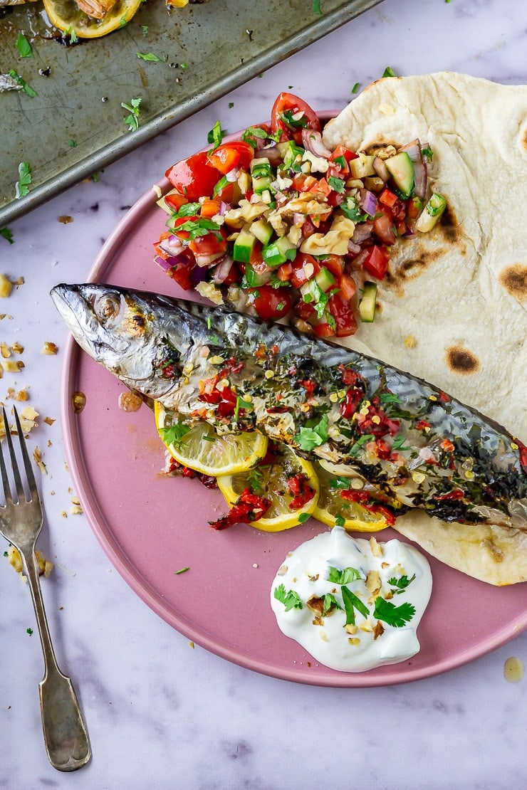 Baked mackerel on a pink plate with salad and flatbread