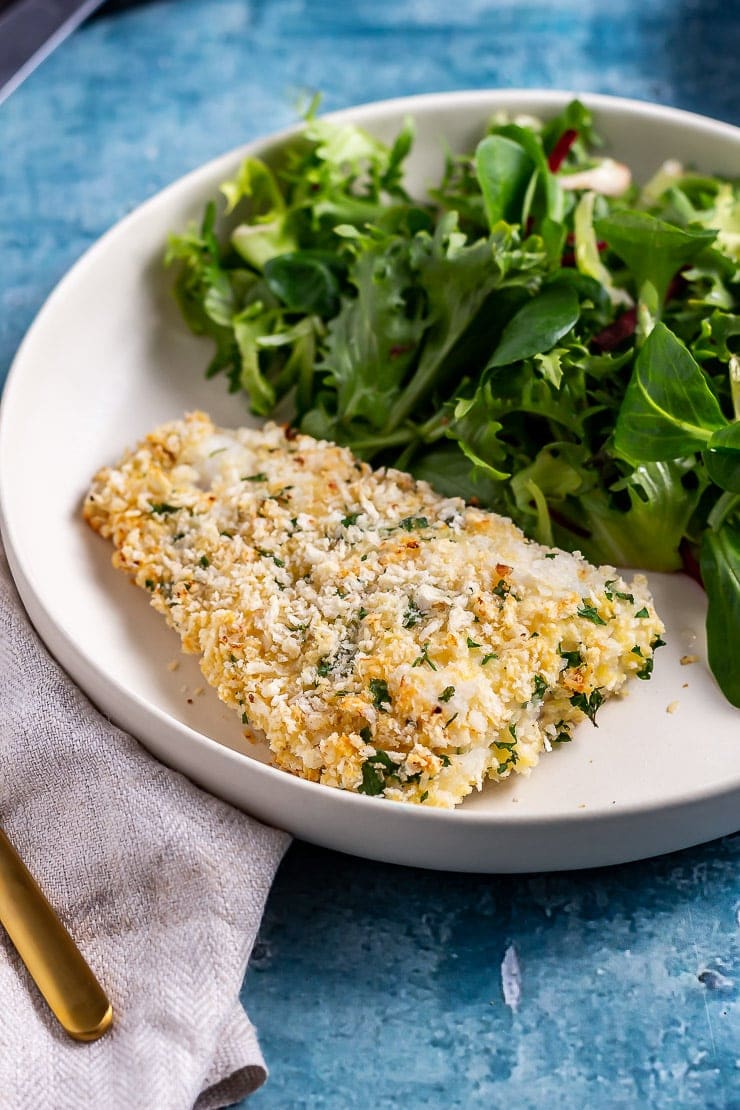 White bowl with breaded fish and salad on a blue background