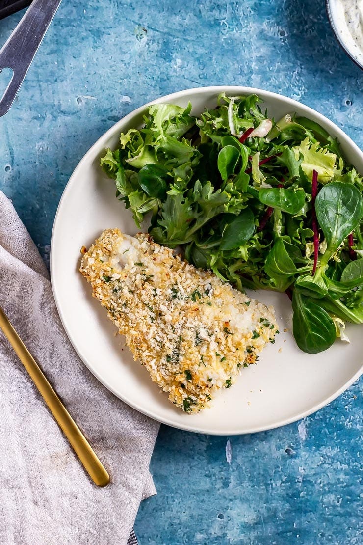 Overhead shot of parmesan breaded fish in a white bowl on a blue background