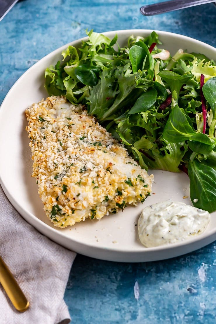 Parmesan breaded fish with salad on a white plate on a blue background