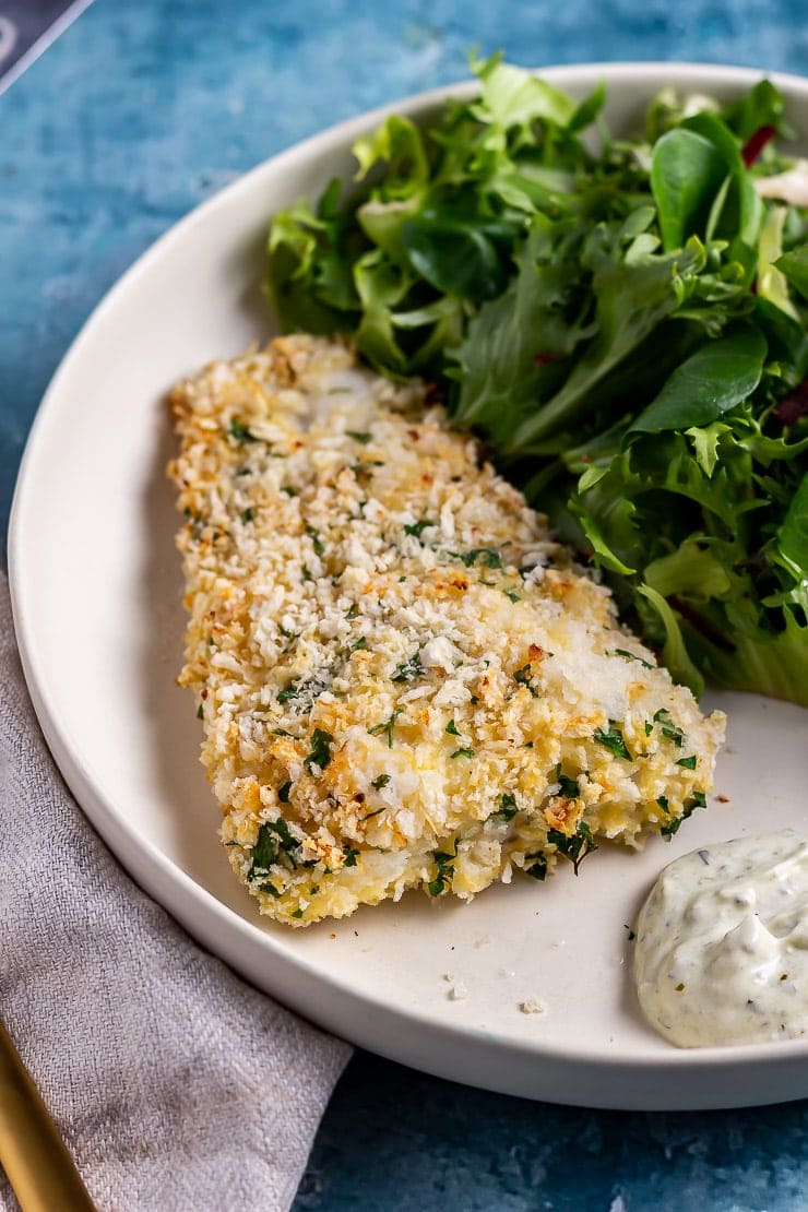 Parmesan breaded fish with salad and yoghurt dip on a white plate