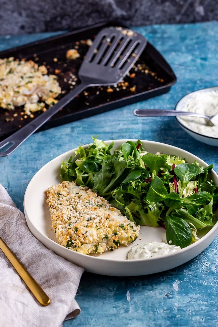 Parmesan breaded fish in a white bowl with salad on a blue background