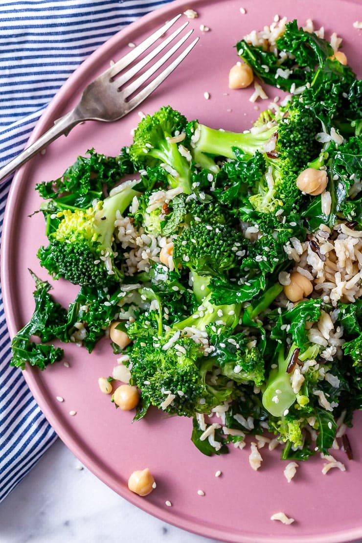 Close up of winter broccoli & wild rice salad on a pink plate with a fork and striped cloth