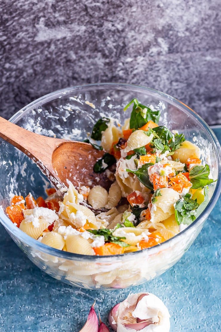 Glass bowl of butternut squash pasta with a wooden spoon