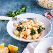 White bowl of roasted butternut squash pasta on a blue background with lemon