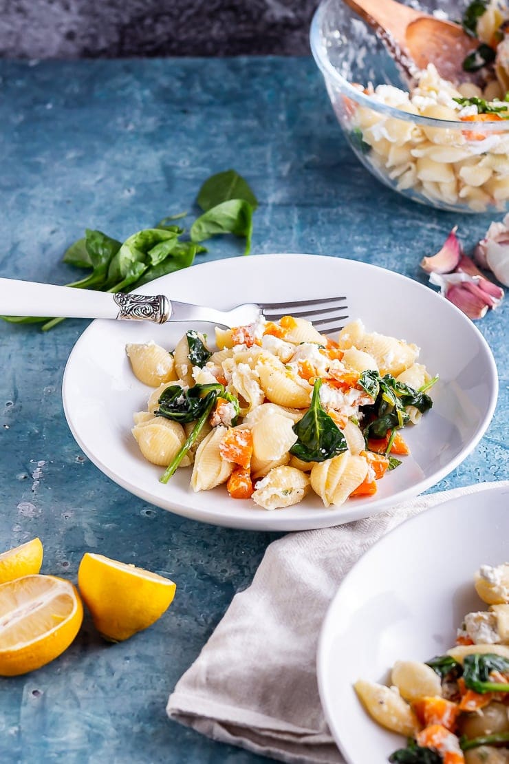 White bowl of roasted butternut squash pasta on a blue background with lemon