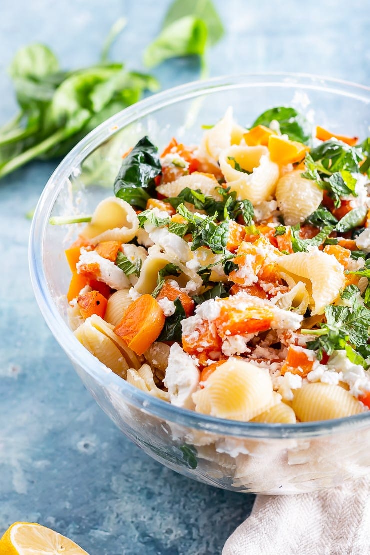 Glass bowl of roasted butternut squash pasta on a blue background with mint and lemon