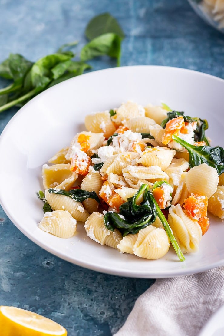 White bowl of butternut squash pasta on a blue background with mint