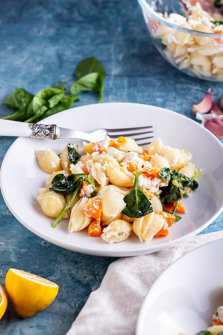 White bowl of butternut squash pasta with a fork and lemon