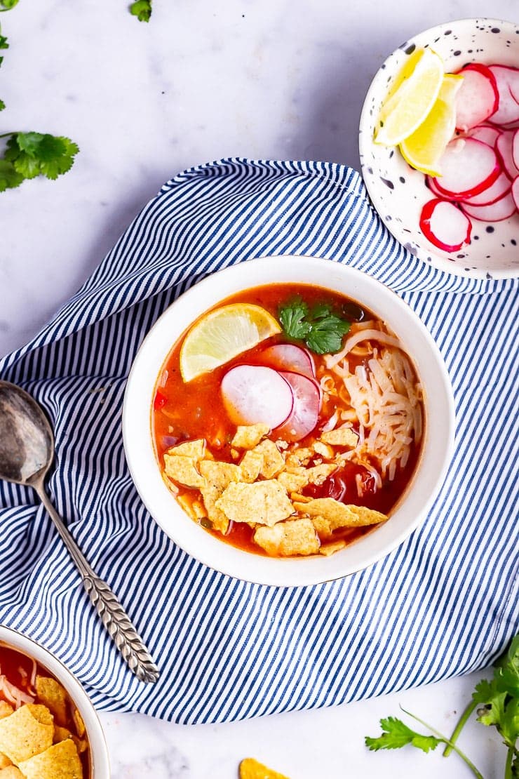 Overhead shot of a bowl of spicy soup on a marble background with a striped cloth