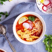 Overhead shot of spicy soup on a striped cloth with lime and coriander