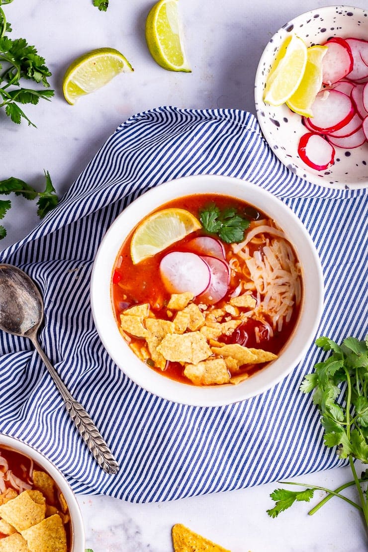 Overhead shot of spicy soup on a striped cloth with lime and coriander