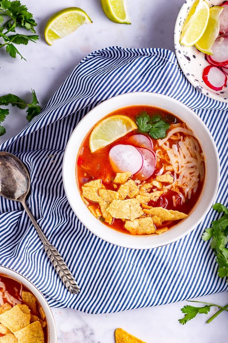 Overhead shot of spicy soup in a white bowl on a striped cloth with toppings