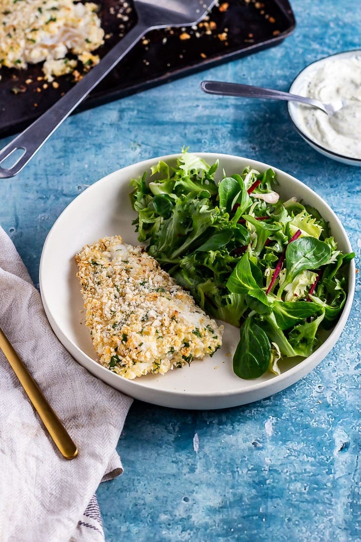 Parmesan breaded fish with salad in a white bowl on a blue background