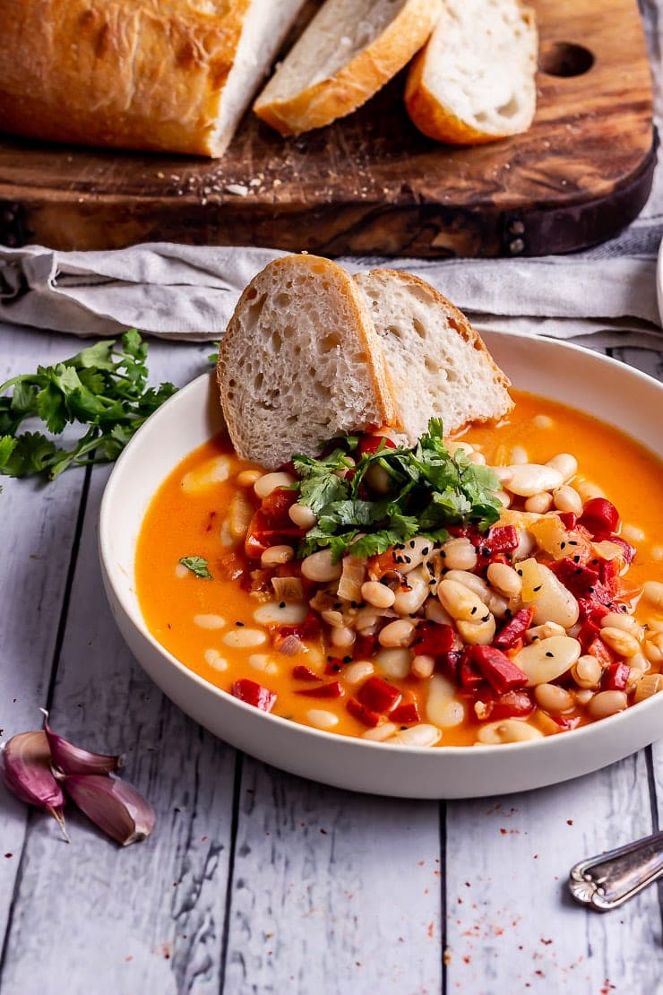 Roasted red pepper soup in a bow with bread on a white wooden surface