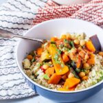 Side on shot of vegetable tagine in a blue bowl with a fork and a cloth in the background