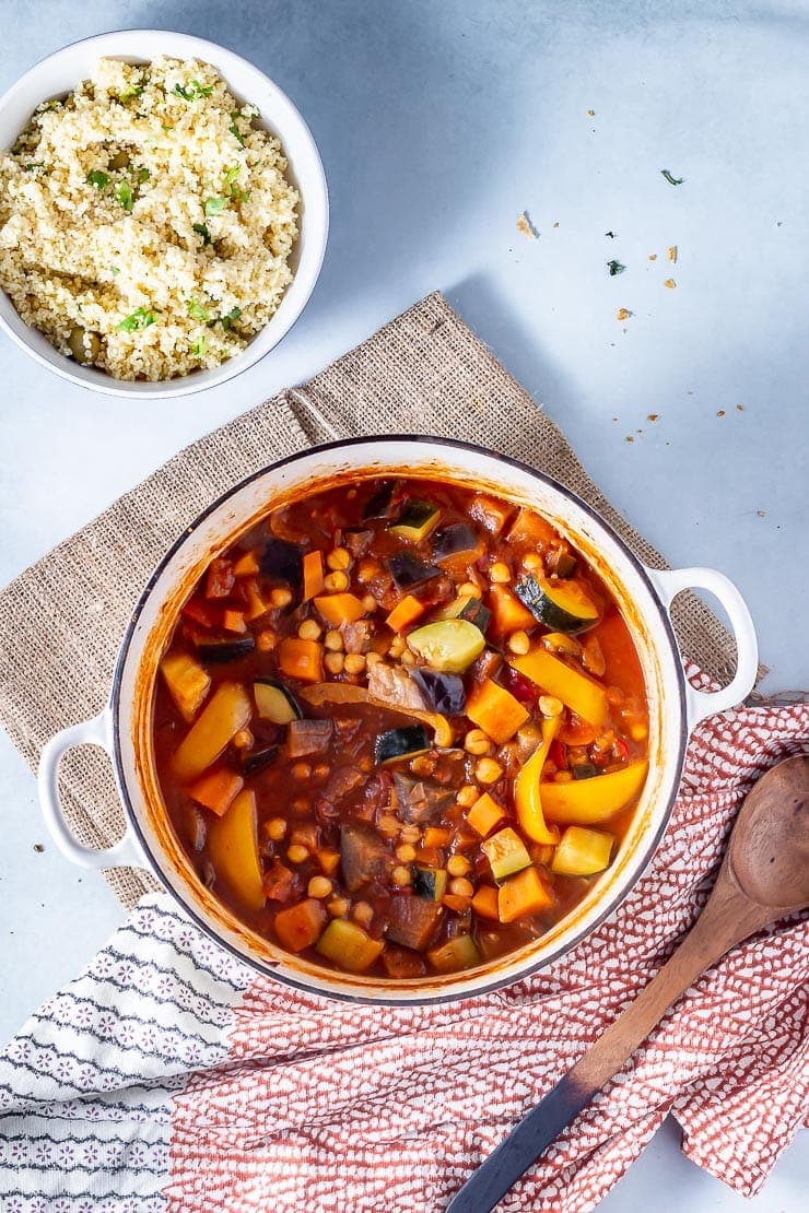 Overhead shot of vegetable tagine with a bowl of couscous on a grey background