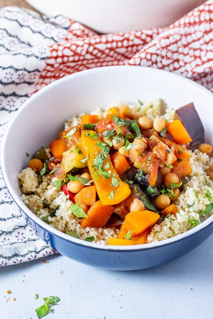 Side on shot of vegetable tagine with couscous in a blue bowl on a grey background