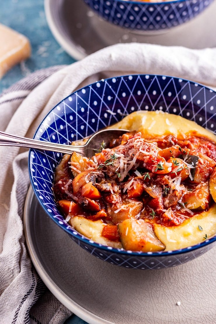 Close up of rich vegetable stew with creamy polenta in a blue bowl with a spoon