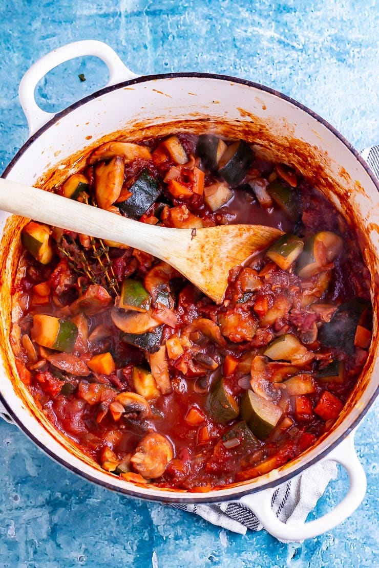 Overhead shot of vegetable stew in a white pot over a blue background